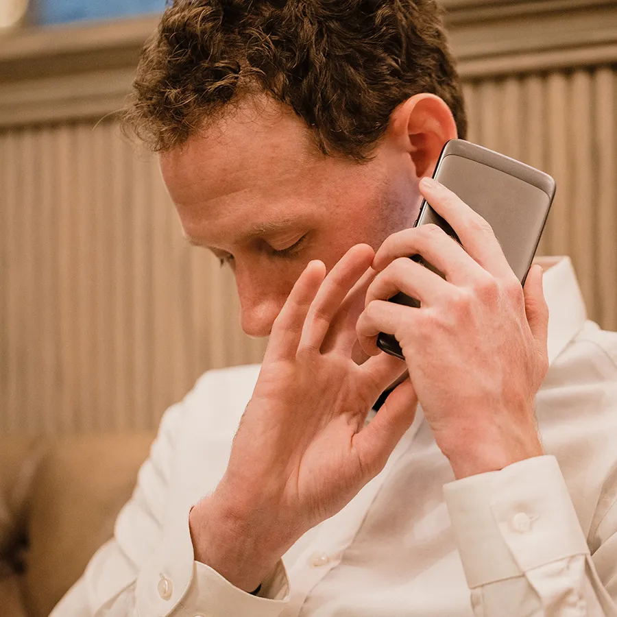 Mann mit weißen Hemd sitzt auf einem braunen Ledersofa und hält ein Smartphone an sein Ohr. Er ist sehbeeinträchtigt und wirkt konzentriert.